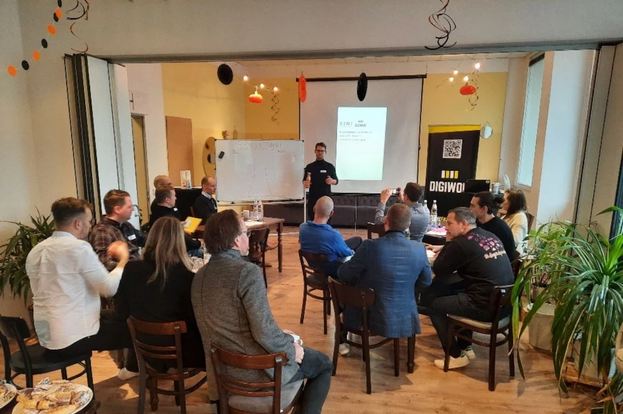 Bei einem Workshop oder Seminar sitzt eine Gruppe von Personen in einem dekorierten Raum vor einem Beamer und hört einem Vortragenden zu.