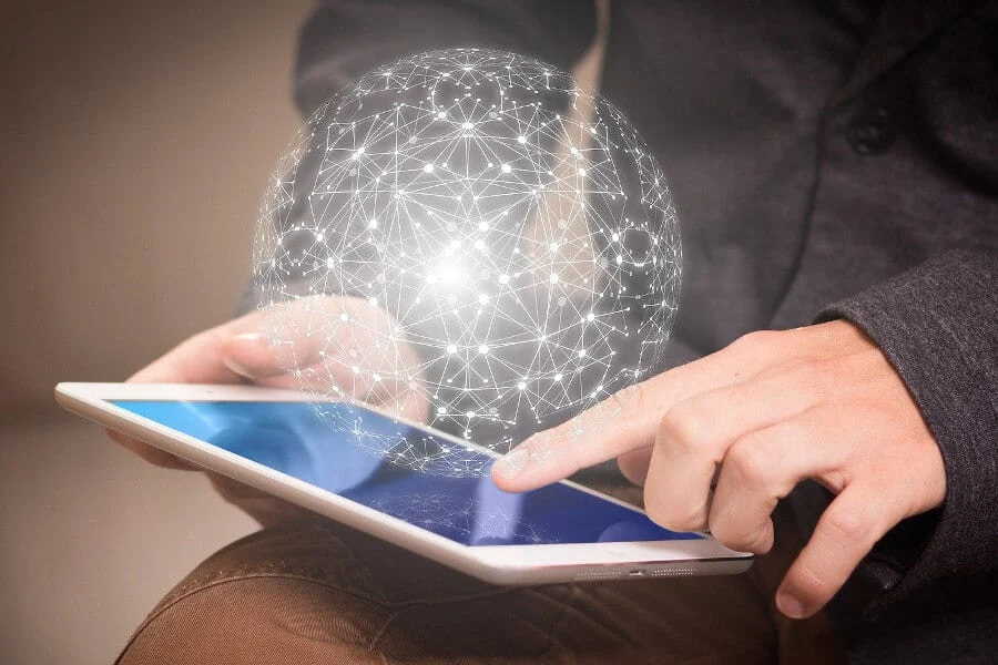 Eine Person benutzt ein Tablet, und über dem Bildschirm erscheint eine digitale leuchtende Kugel aus miteinander verbundenen Linien und Knotenpunkten.