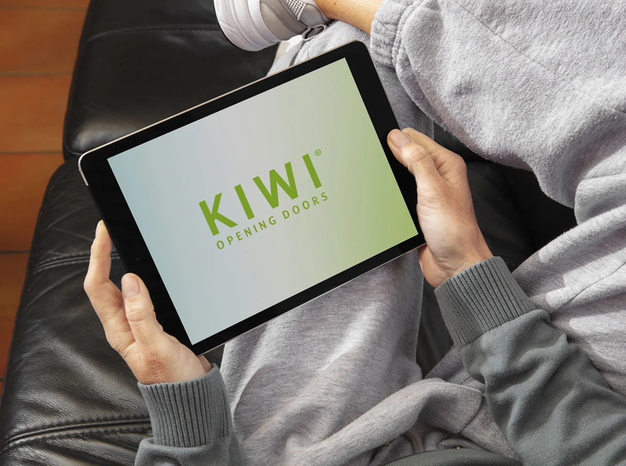 Person nutzt gemütlich auf dem Sofa ein Tablet mit dem KIWI-Logo – symbolisiert digitalen Zugang und benutzerfreundliche Steuerung des Zutrittssystems.