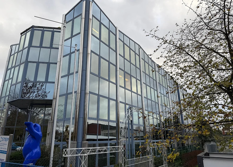 modernes Bürogebäude mit Glasfassade am Standort Estavio, davor blaue Skulptur und Eingangsbereich von KIWI