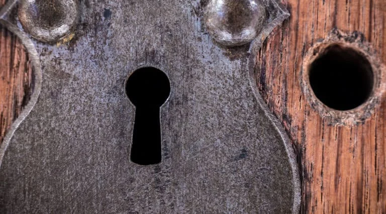 Nahaufnahme einer alten Metall-Schlüssellochplatte auf einer hölzernen Oberfläche, mit einem runden Loch daneben.