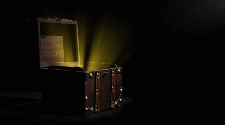 Eine alte Holztruhe mit Metallakzenten steht offen und strahlt vor einem dunklen Hintergrund ein helles gelbes Licht aus.