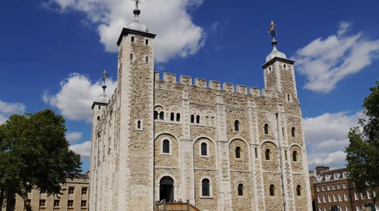Das Bild zeigt den White Tower, eine historische Steinfestung mit vier Ecktürmen, die zum Tower of London gehört, unter einem blauen Himmel mit vereinzelten Wolken.