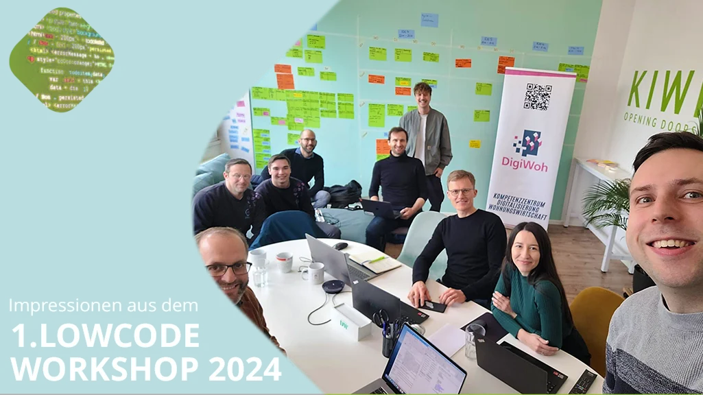 Eine Gruppe von acht Personen sitzt und steht in einem Workshop mit Laptops um einen Tisch herum und lächelt für ein Gruppen-Selfie; bunte Notizen bedecken die Wand hinter ihnen.