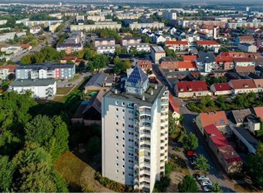 Luftaufnahme eines Wohnhochhauses mit markanter Glaskuppel, umgeben von Einfamilienhäusern, Bäumen und weiteren Wohngebäuden in einem Stadtteil