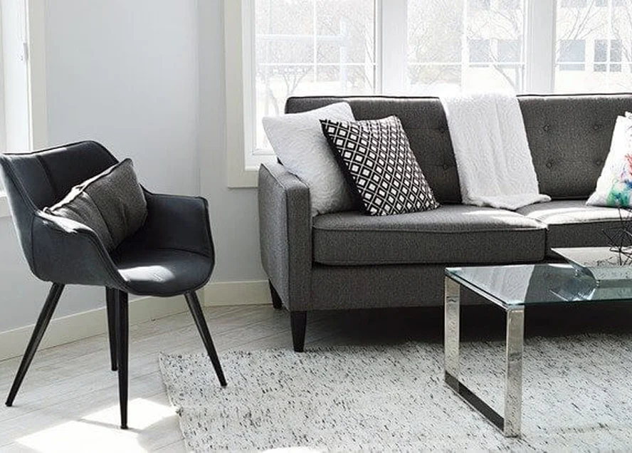 Helles Wohnzimmer mit grauem Sofa, Designerstuhl und Glastisch im skandinavischen Stil